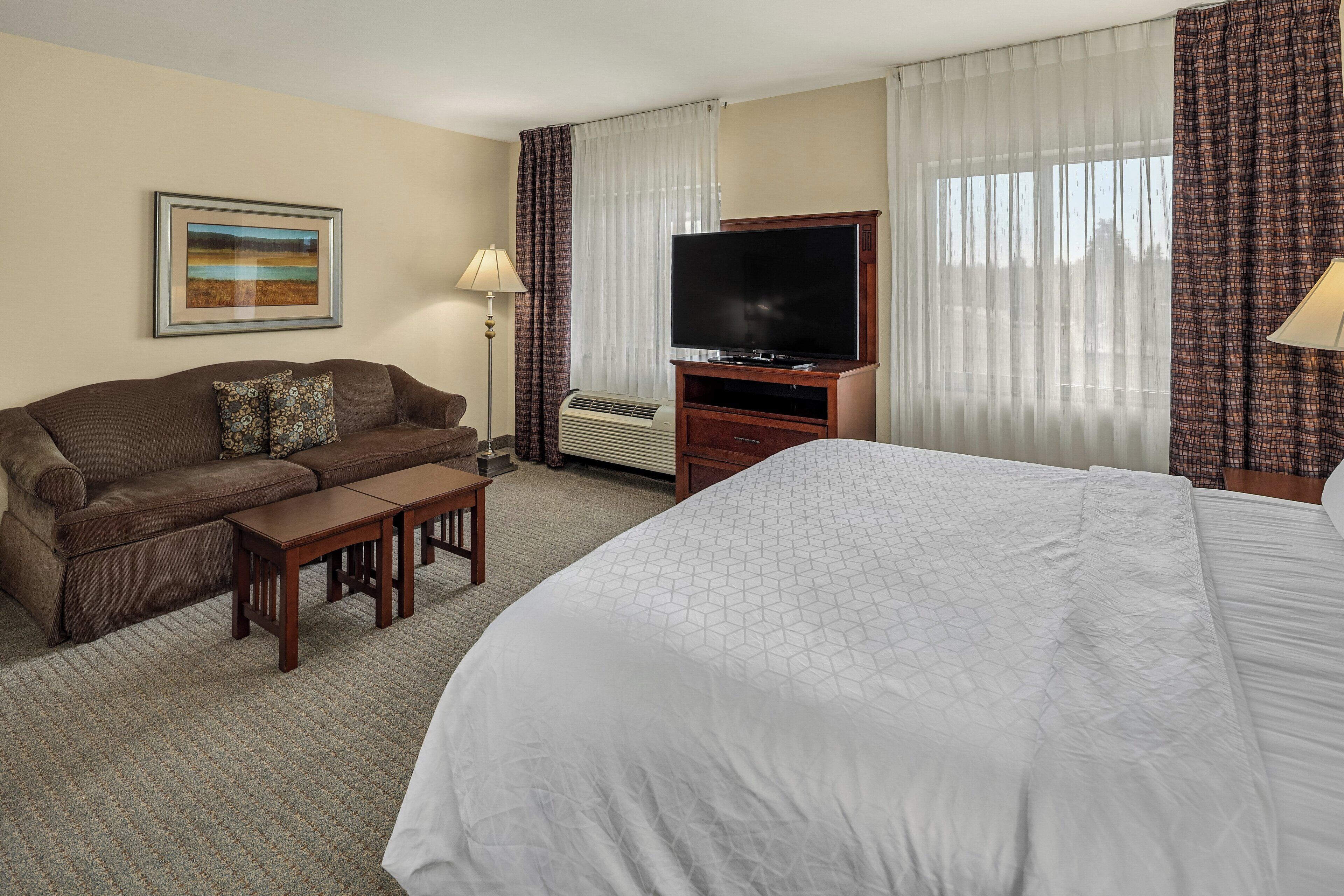 A hotel room with a bed, a sofa, a TV, and a painting on the wall.