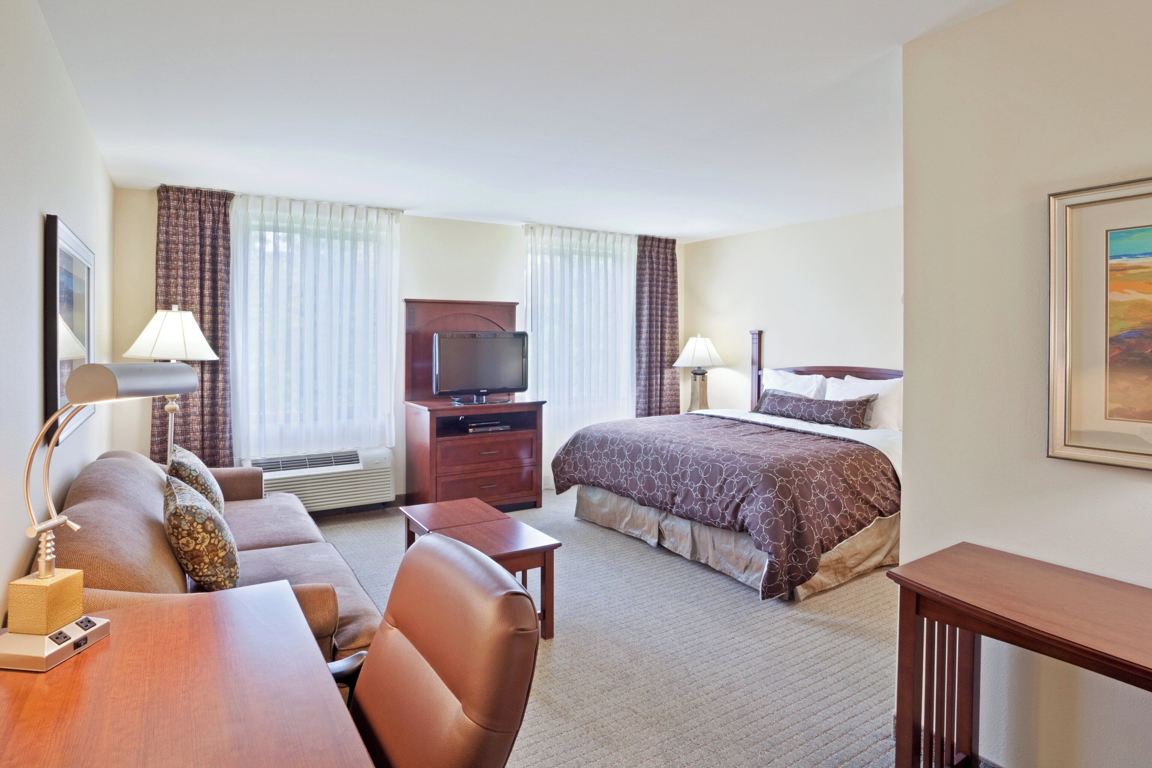 Habitación de hotel con cama, escritorio, televisor, cómoda y un cuadro en la pared.