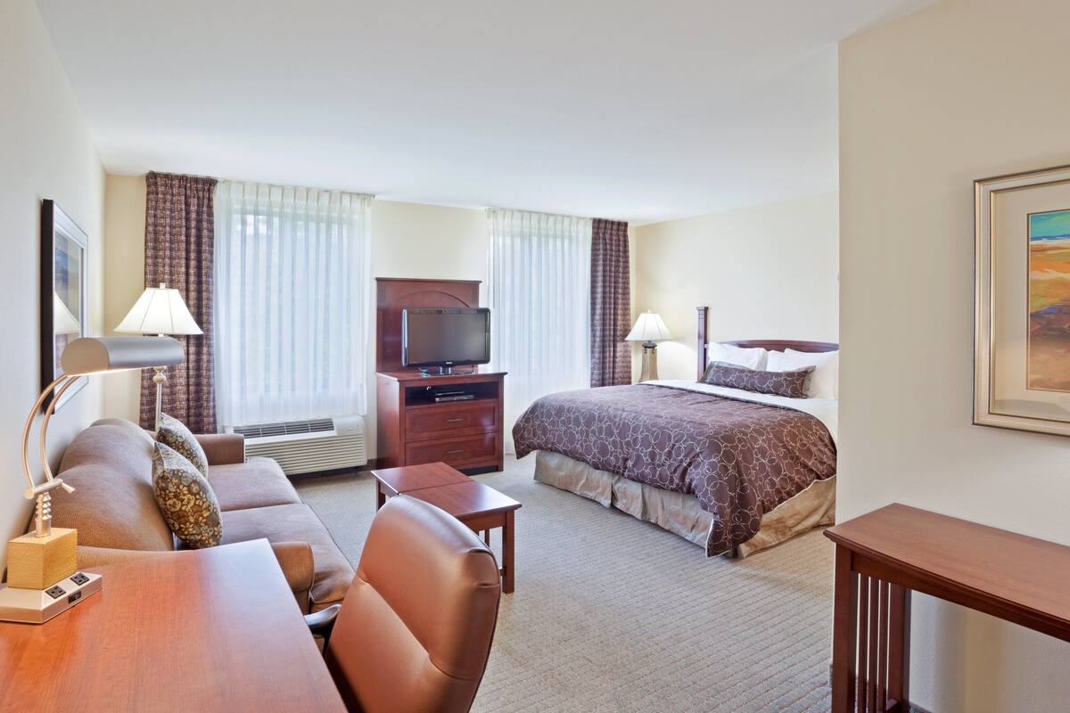 A hotel room with a bed, a desk, a chair, a television, and a window with curtains.