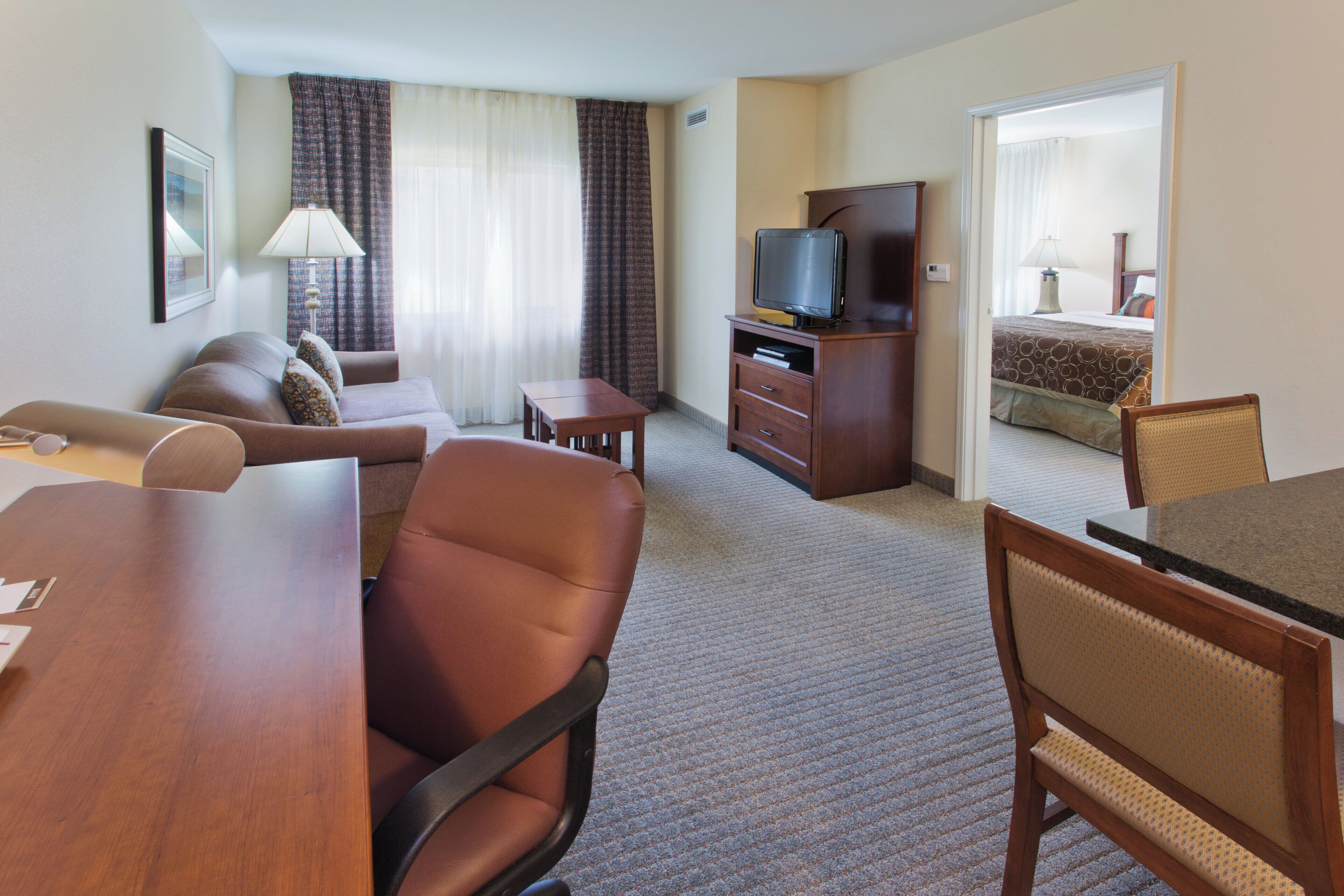 Ein Hotelzimmer mit einer Couch, einem Esstisch, einem Fernseher auf einer Holzkommode und einem Bett mit einem gemusterten Bettbezug.