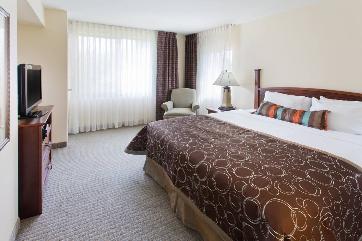 A hotel room with a large bed, a chair, a desk with a television, and curtains.