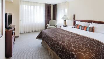 A hotel room with a large bed, a chair, a desk with a television, and a lamp.