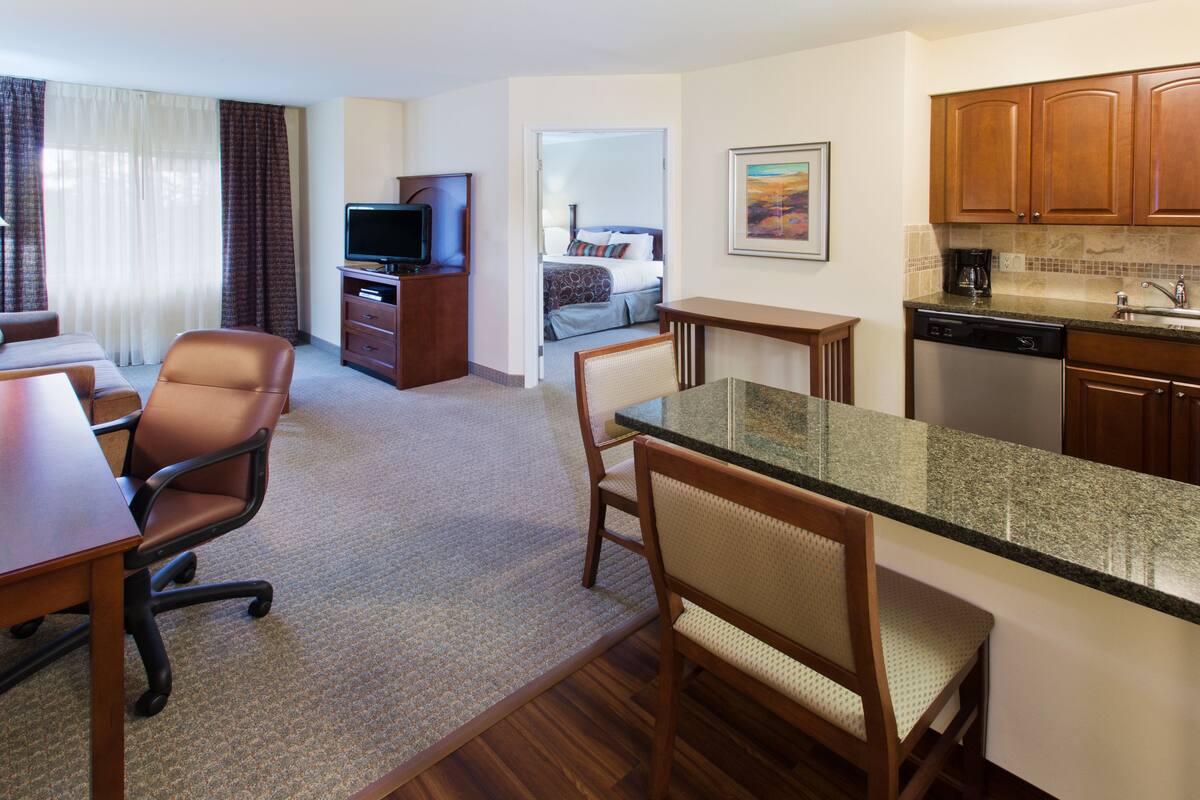 A hotel room with a dining area, a kitchen, a TV, and a bed.