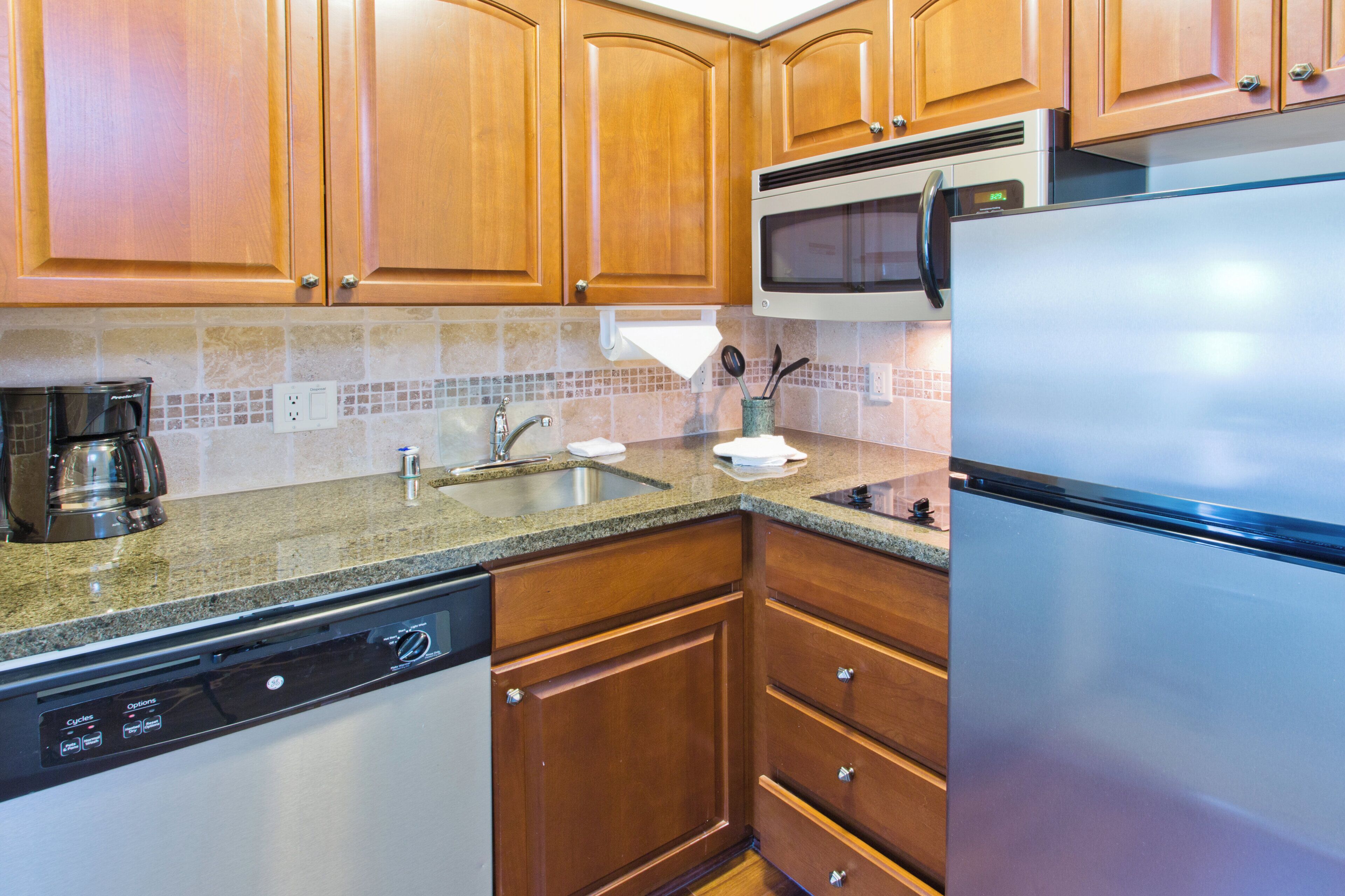A kitchen with wooden cabinets, a stainless steel refrigerator, a microwave, a dishwasher, and a granite countertop.