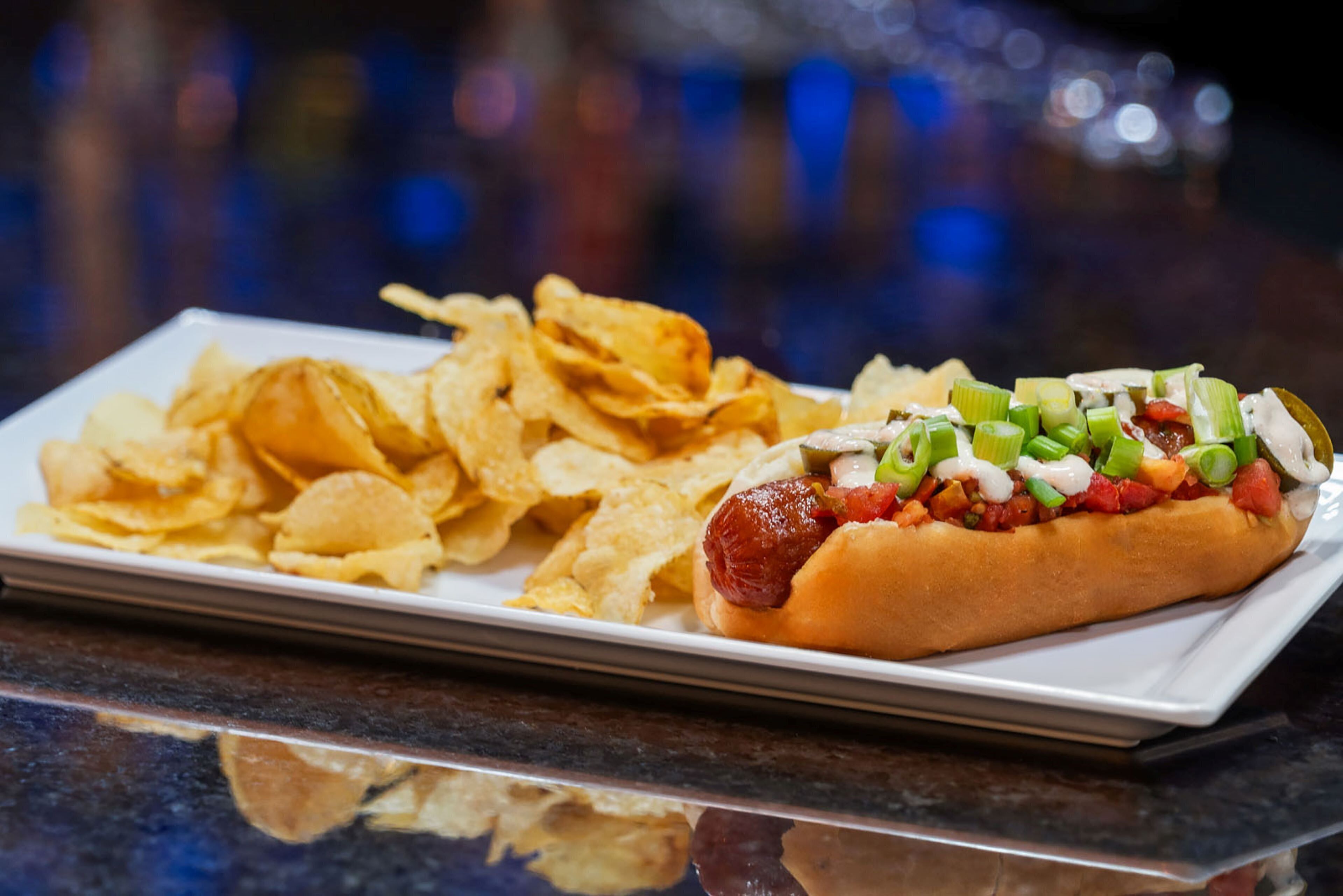 Ein Hotdog mit Belag und Pommes auf einem weißen Teller.