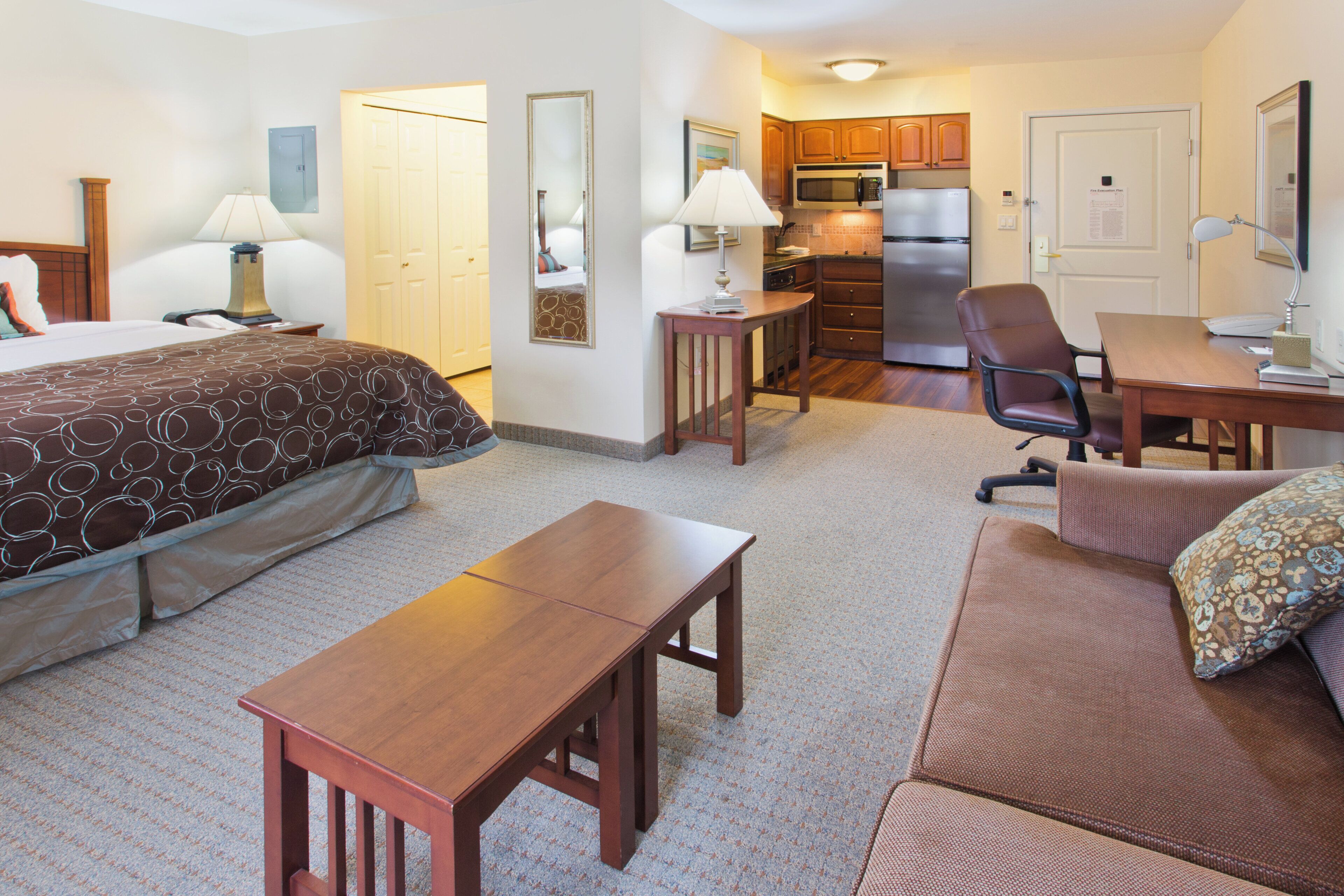 A hotel room with a bed, a desk, a chair, a sofa, a small table, and a kitchenette.