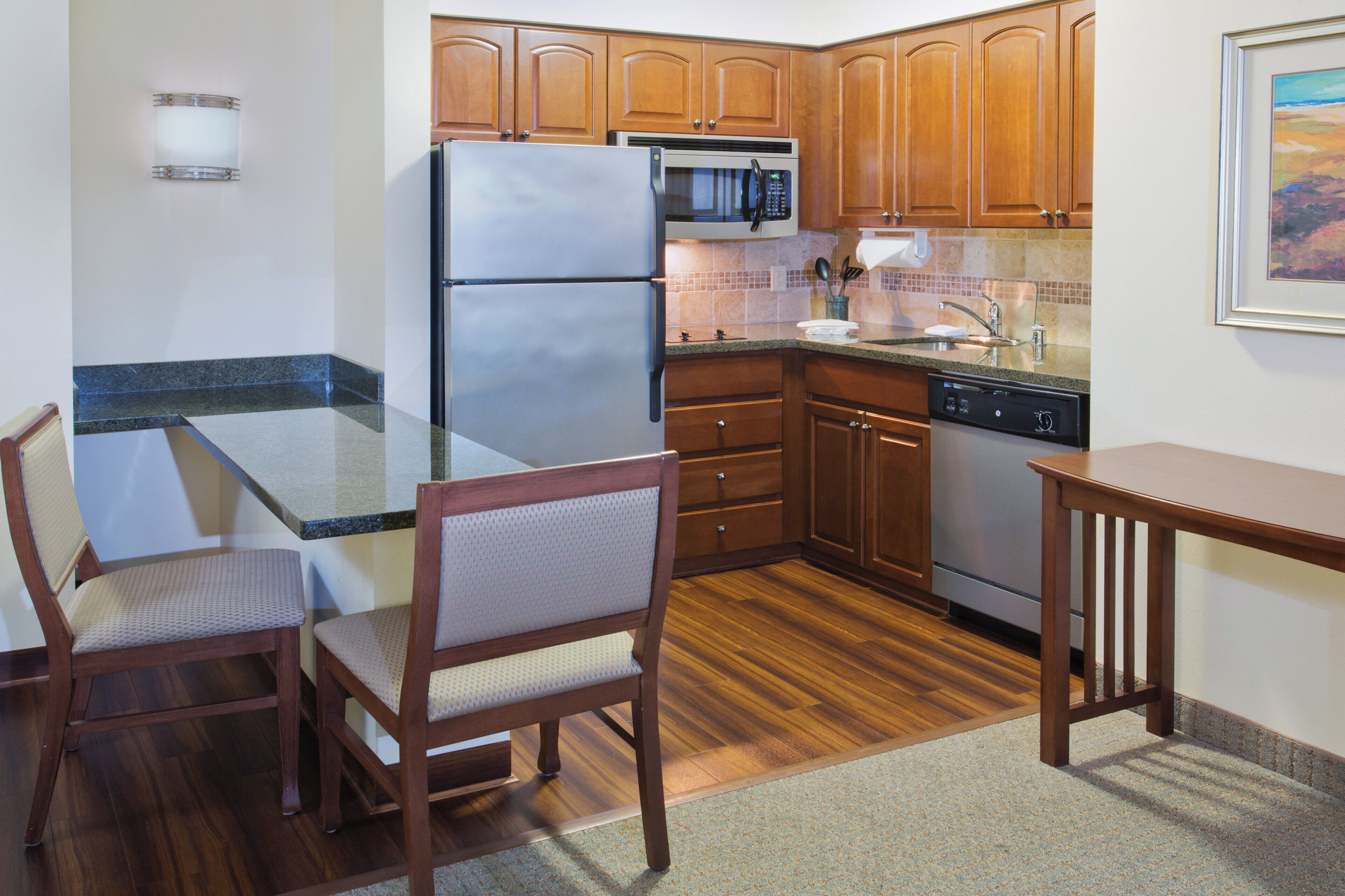 Una cocina compacta con muebles de madera, un refrigerador de acero inoxidable, un microondas y un lavavajillas.