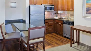 Cocina con armarios de madera, un refrigerador de acero inoxidable, un microondas y un lavavajillas. Hay una mesa de comedor con sillas y una alfombra en el suelo.