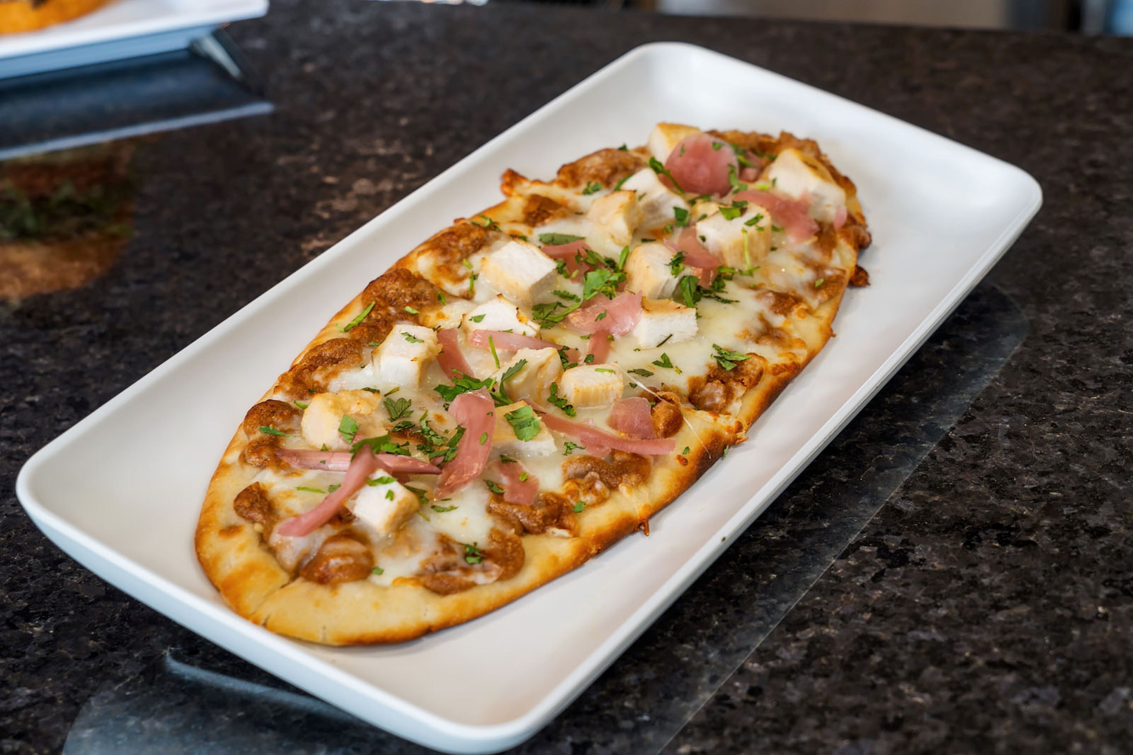 A rectangular white plate with a rectangular food item, possibly a pizza, on a dark granite countertop.