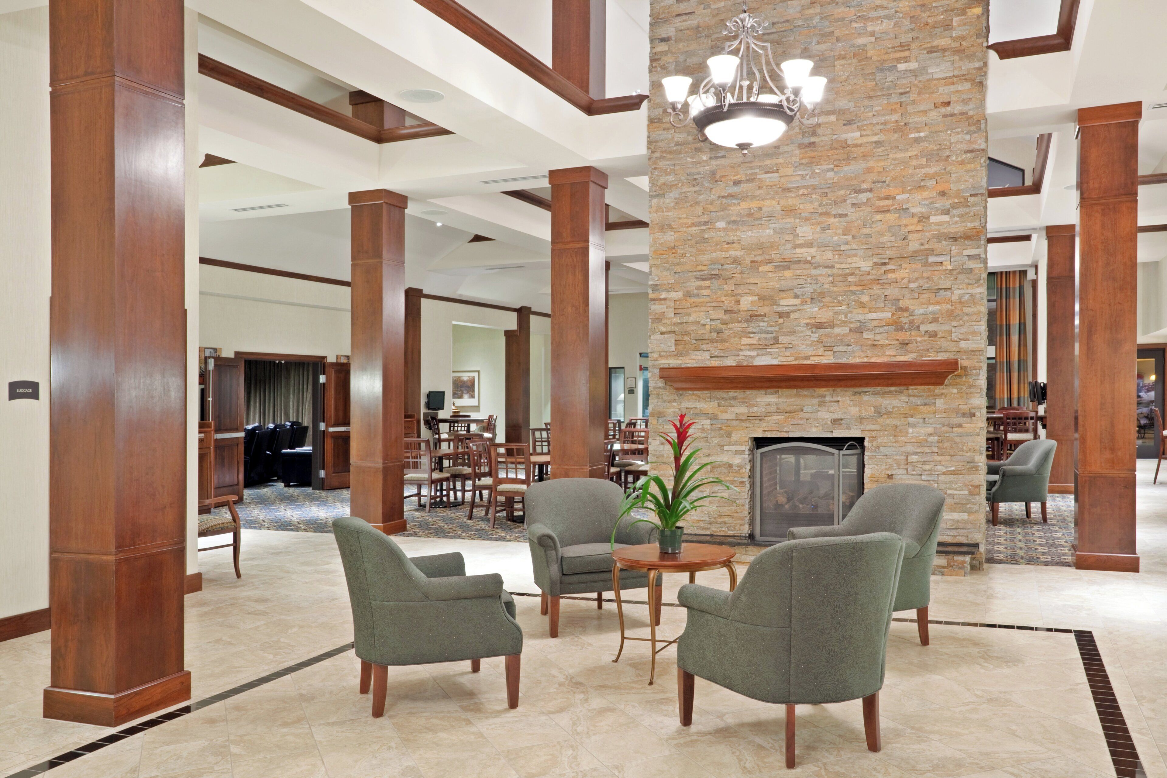 A spacious lobby with high ceilings, wooden columns, and a stone accent wall. There is a seating area with chairs and a table, and a fireplace.