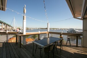 A wooden deck with a table and chairs, overlooking a marina with boats and a clear sky.