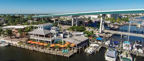 A marina with docked boats, a covered area with umbrellas, and a bridge in the background.