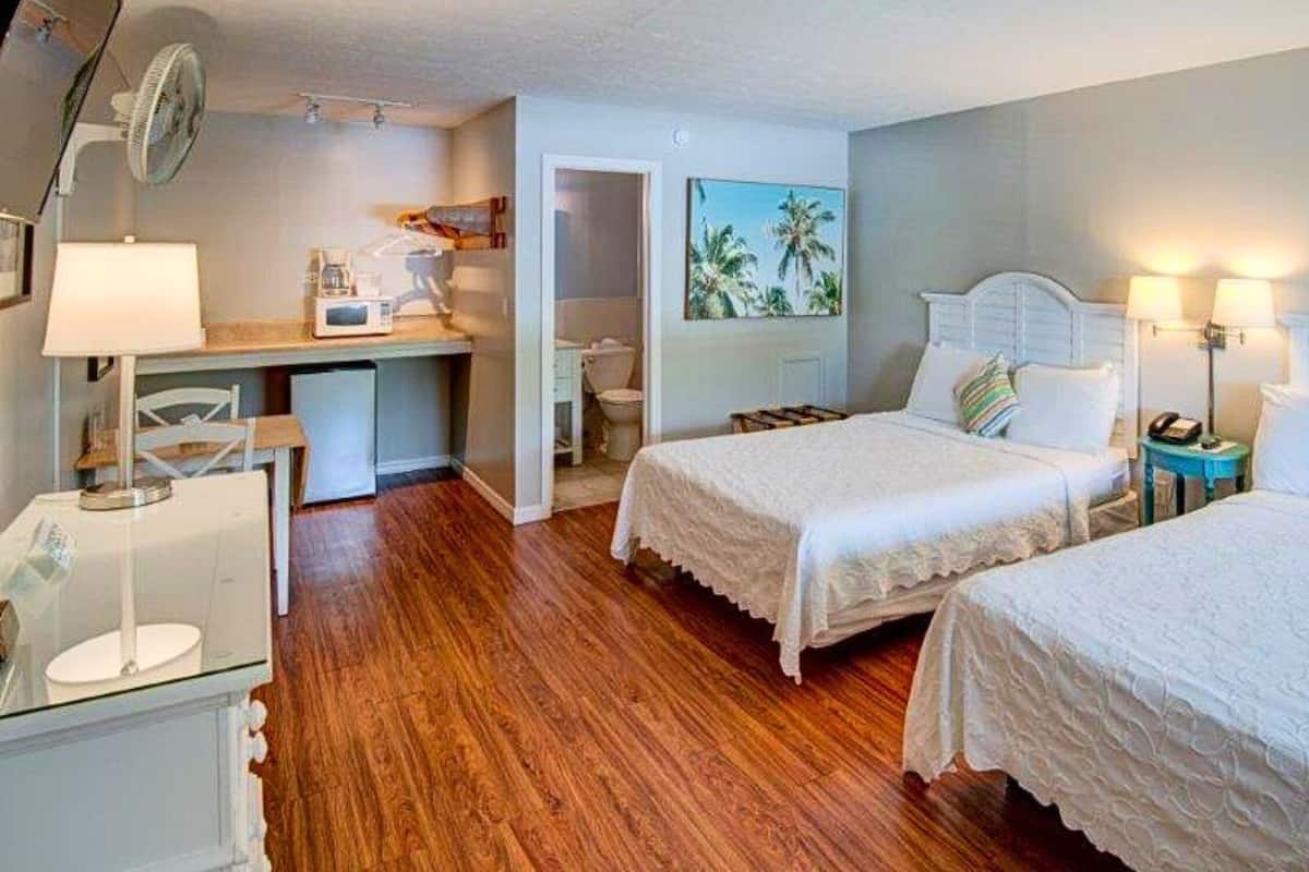 Habitación de hotel con dos camas, un escritorio con silla, una mesita y un ventilador.