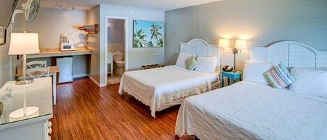 Une chambre d’hôtel avec deux lits, un bureau avec une chaise, une petite table et un ventilateur.