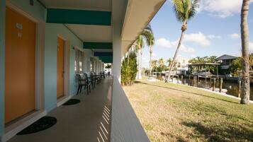 A hotel corridor with doors numbered 131 and 132, outdoor seating, palm trees, and a view of a dock with boats.