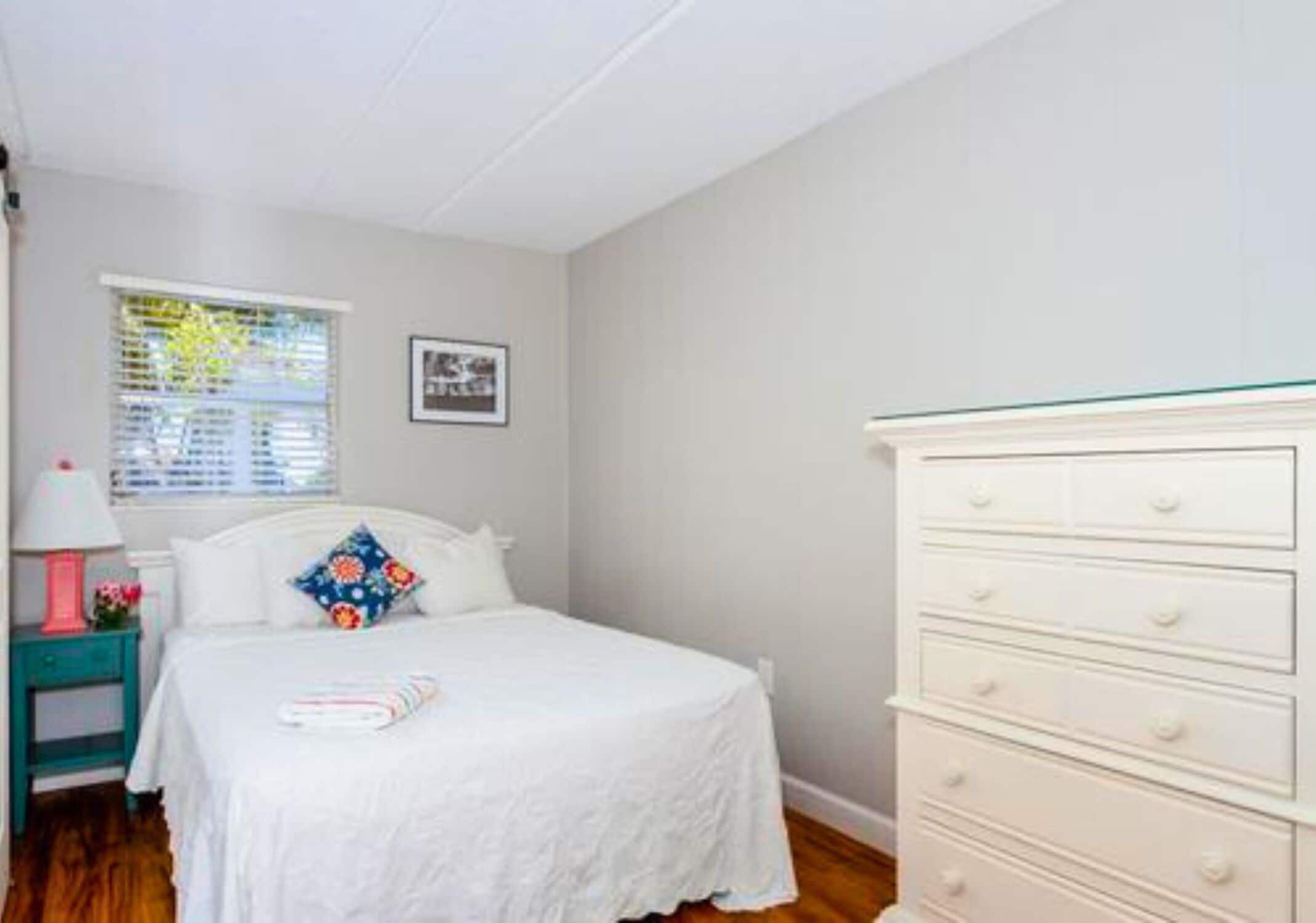 A bedroom with a bed, a dresser, a nightstand, a window with blinds, and a framed picture on the wall.