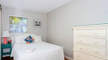 A bedroom with a bed, a dresser, a nightstand, a window with blinds, and a framed picture on the wall.
