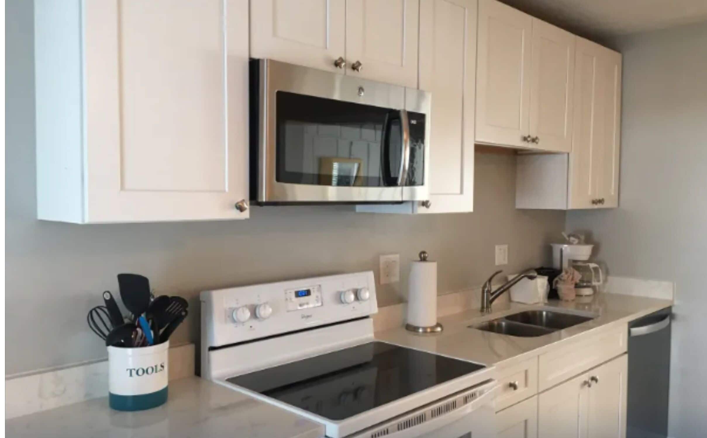 A modern kitchen with white cabinets, a built-in microwave, a stove, and a sink.