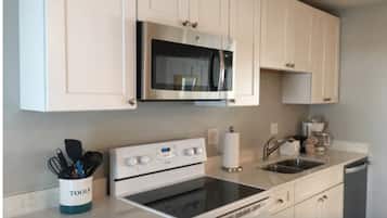 A modern kitchen with white cabinets, a built-in microwave, a stove, and a sink.