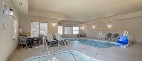 An indoor swimming pool with a lounge area, chairs, and a table.