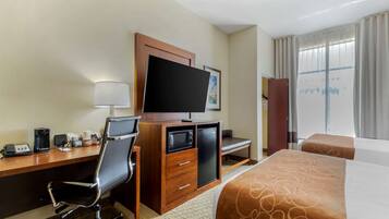 A hotel room with a desk, chair, television, microwave, and two beds.
