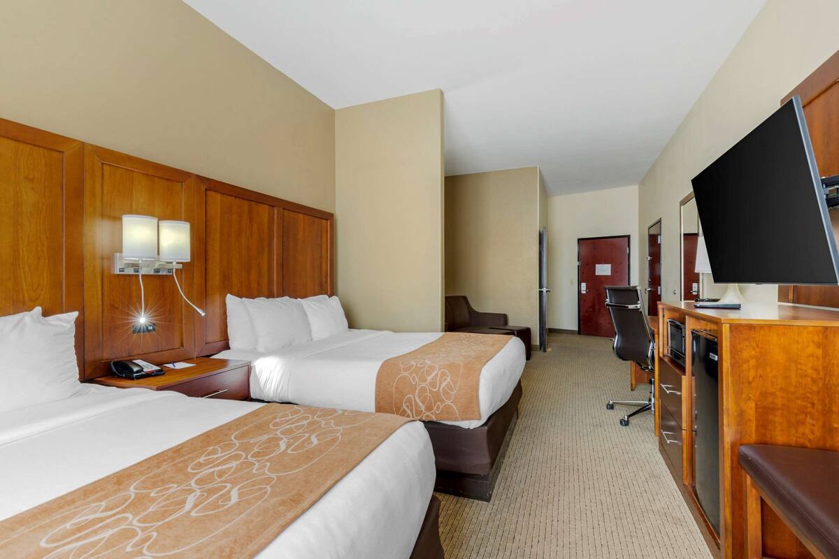 A hotel room with two beds, a desk with a computer, a TV, and a minibar.