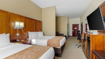 A hotel room with two beds, a desk with a computer, a TV, and a minibar.