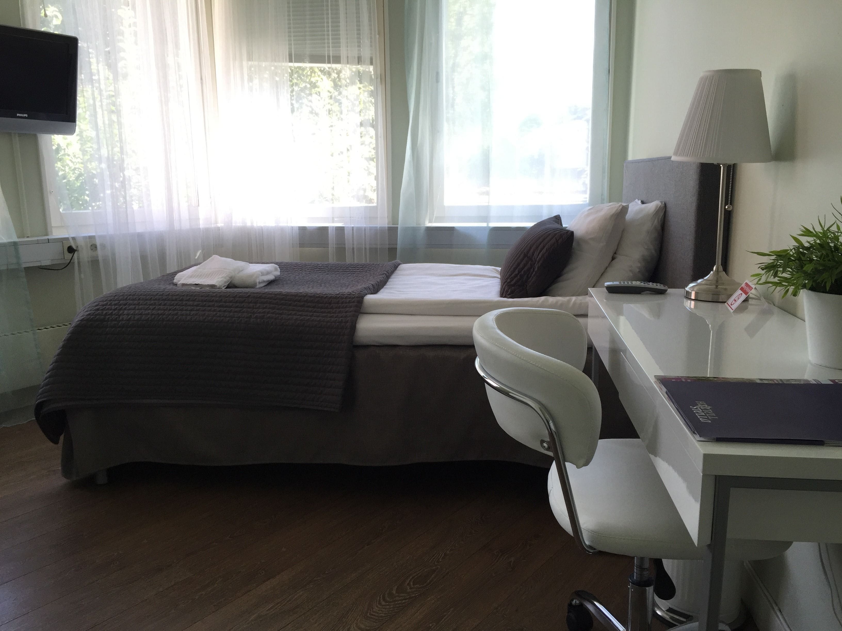 Una habitación de hotel con cama, escritorio, silla, lámpara y televisión.