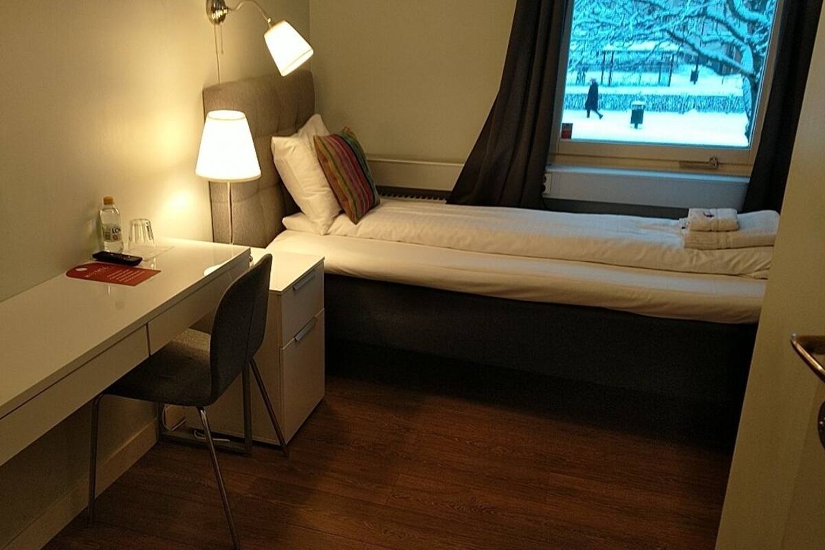 A compact hotel room with a single bed, a desk, and a chair.