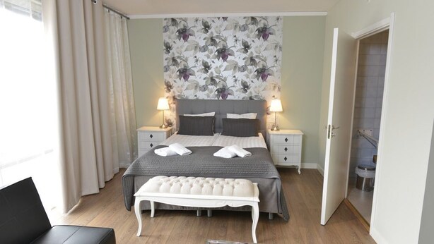 A bedroom with a bed, bedside tables, a bench, and a view of the bathroom. - Hotell Stella (Uppsala)
