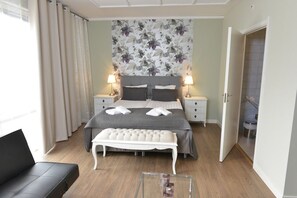 A bedroom with a bed, bedside tables, a bench, and a view of the bathroom. - Hotell Stella (Uppsala)