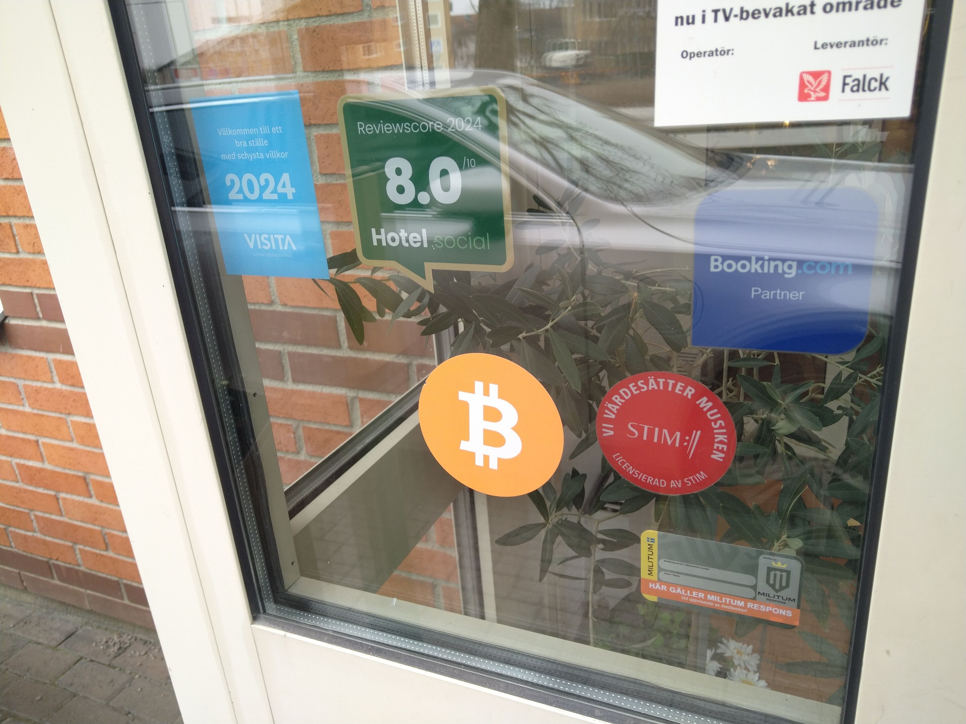Een raam met verschillende stickers, waaronder een 2024 VISITX sticker, een Hotel Social score van 8.0, een Bitcoin symbool en een STIM:11 sticker.