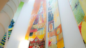 A brightly lit atrium with a large, colorful mural of a building. - Hotell Stella (Uppsala)