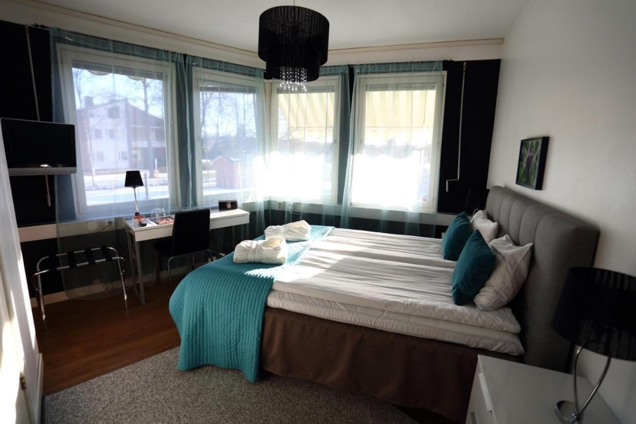 Ett hotellrum med en säng, ett skrivbord, en stol, en tv och ett fönster med gardiner.