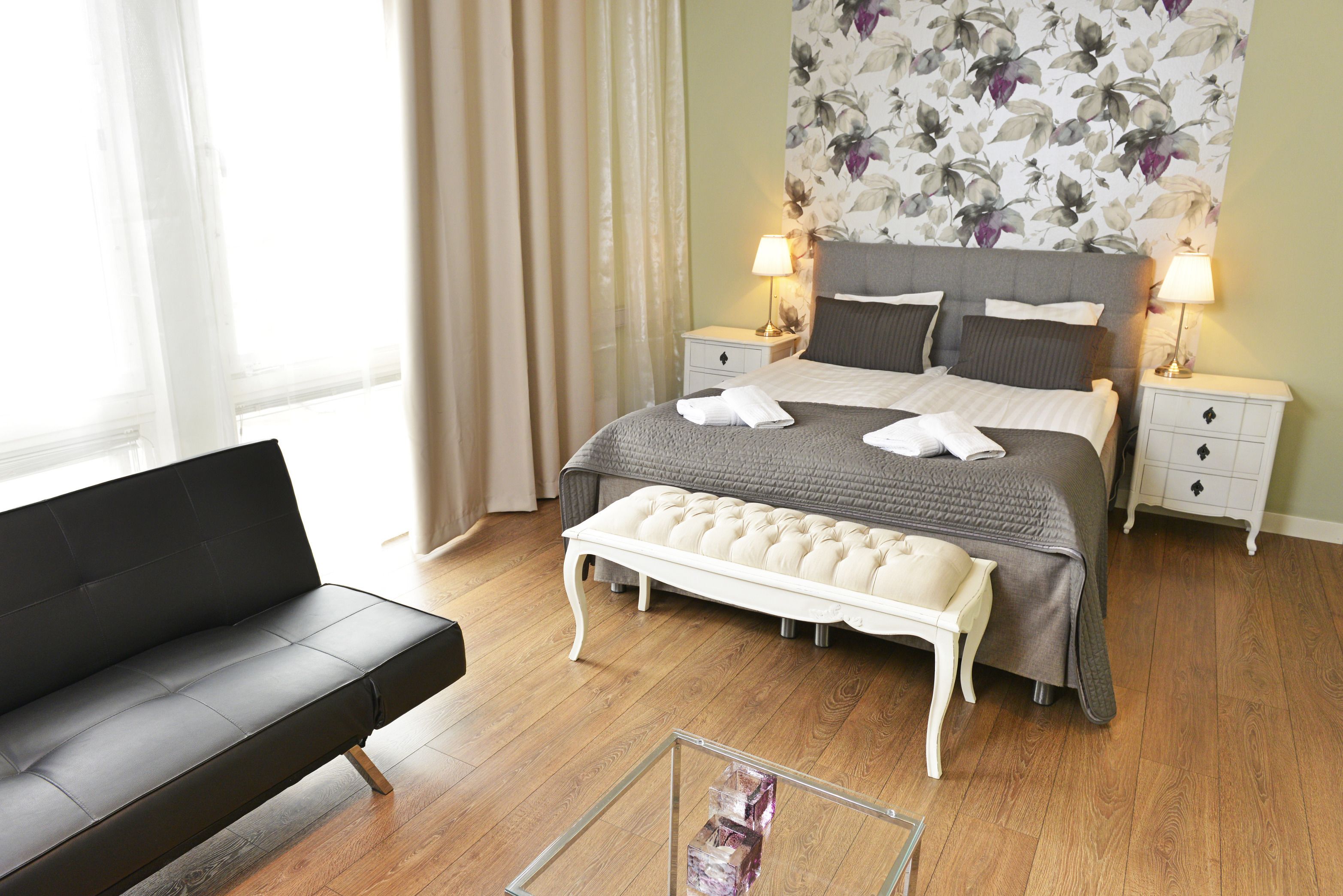 Una habitación de hotel moderna con una cama, mesitas de noche, un banco, un sofá y un amplio papel tapiz floral.