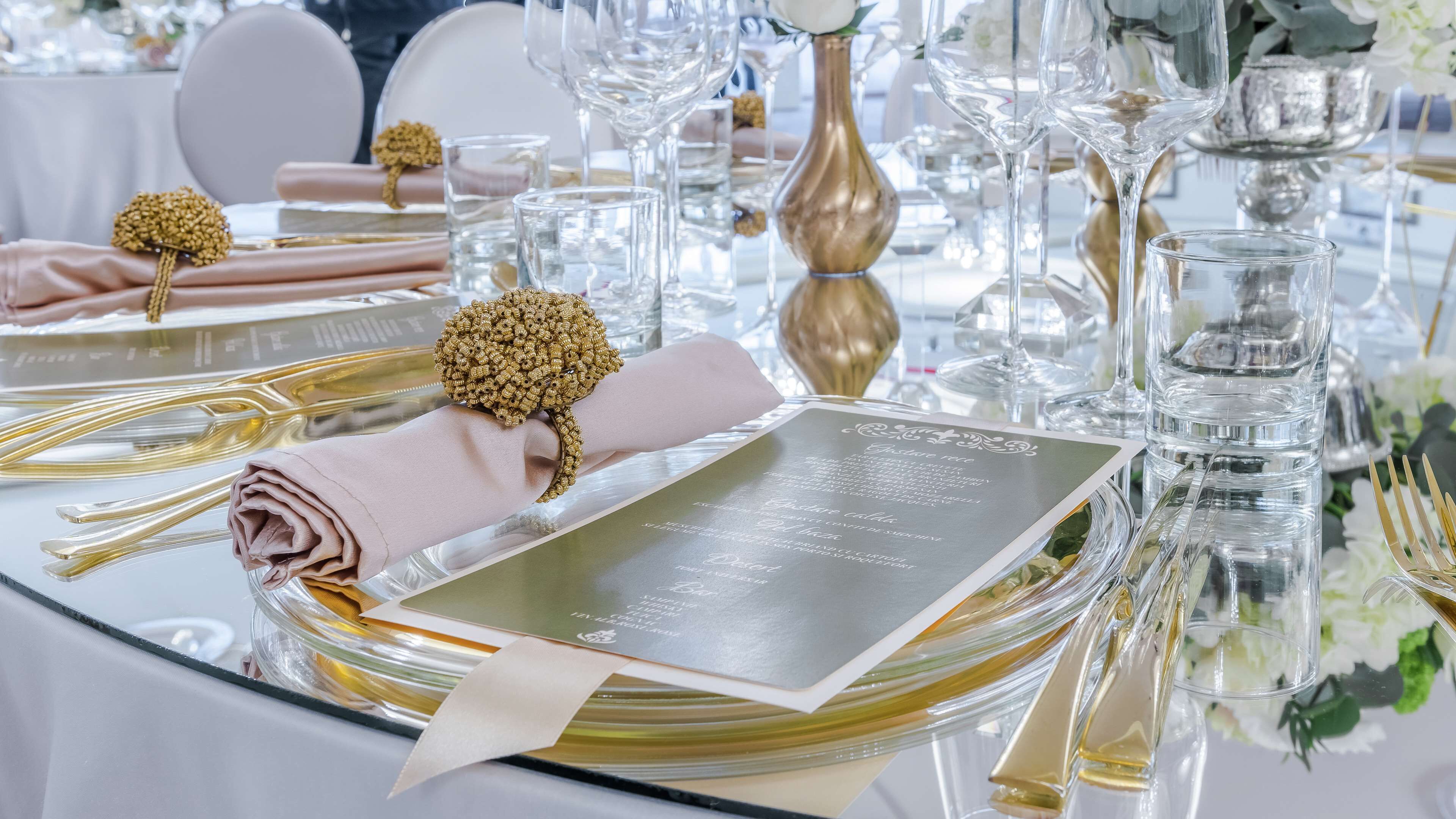 A table set with gold and pink linens, clear glassware, and a menu.