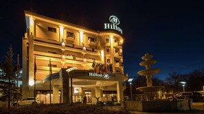 A multi-story hotel with a prominent Hilton sign, a fountain, and flags in front.
