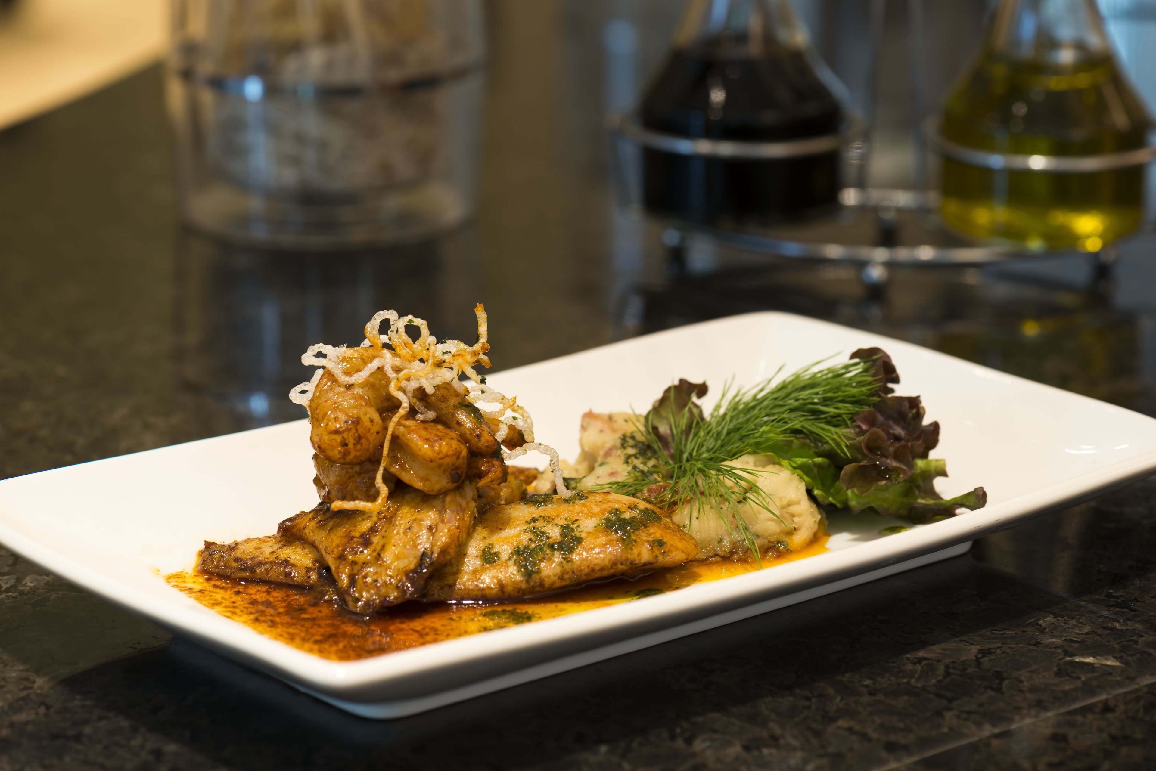 A white rectangular plate with a fish dish, garnished with herbs and onions, on a dark countertop.