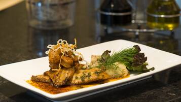 A white rectangular plate with a fish dish, garnished with herbs and onions, on a dark countertop.