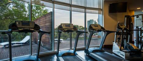 A gym with treadmills, a TV, and large windows overlooking a brick patio.