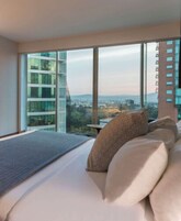 Una habitación de hotel moderna con una cama grande, vistas a la ciudad y ventanas amplias.