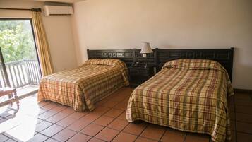 Una habitación con dos camas, una ventana con cortinas, aire acondicionado y una mesita de noche con lámpara.