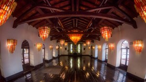 Un salón espacioso con techo alto y vigas de madera, que incluye múltiples candelabros y arcos.