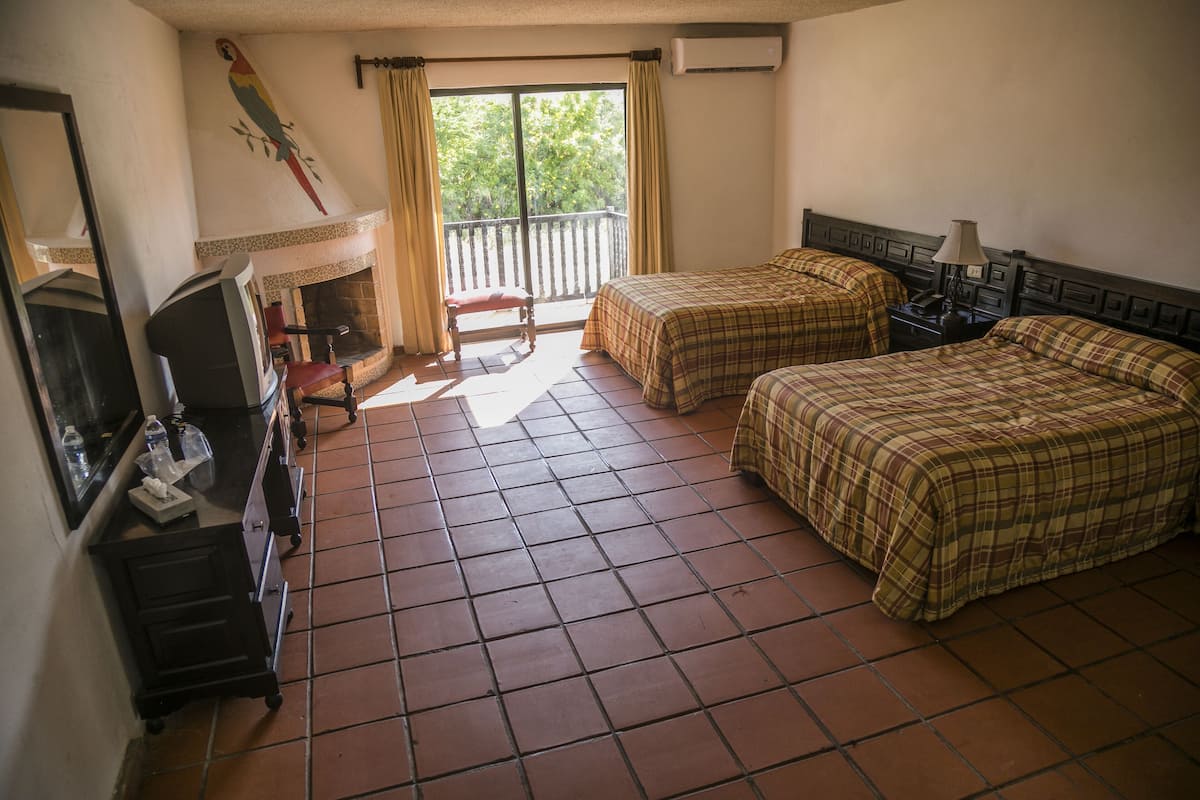 Habitación de hotel con dos camas, televisor, chimenea y balcón con cortinas.