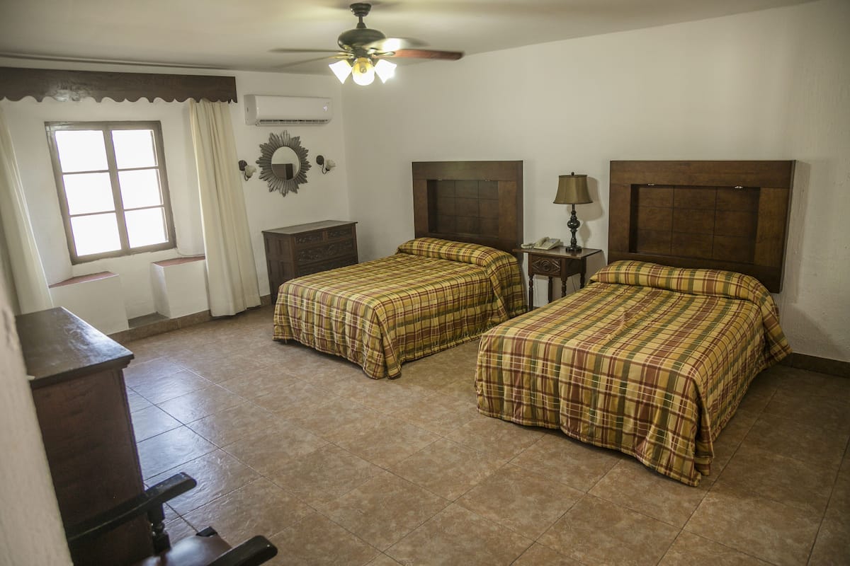 Un dormitorio con dos camas, un ventilador de techo, una ventana con cortinas, un aparador y un espejo en la pared.
