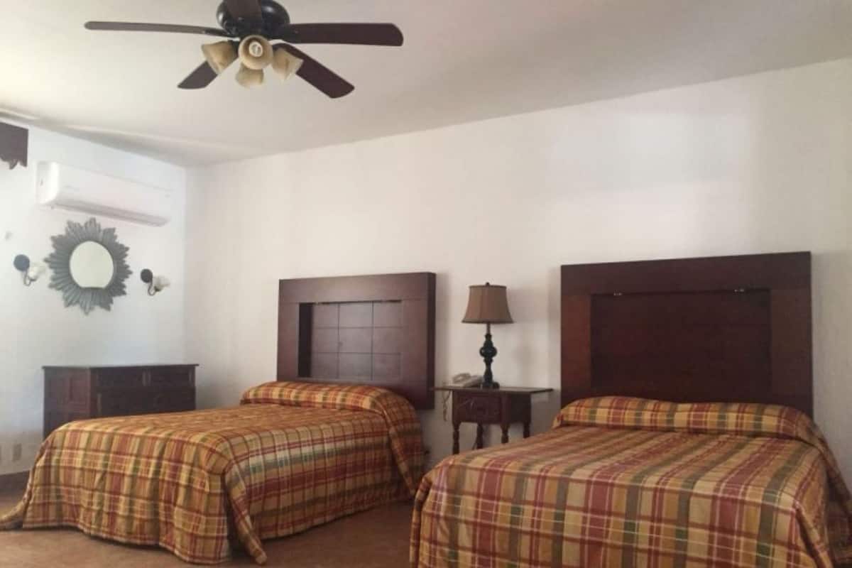 Una habitación con dos camas, un ventilador de techo, un espejo y una lámpara.