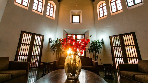 Un vestíbulo amplio con una gran mesa de madera, varios sofás y un jarrón de flores rojas.
