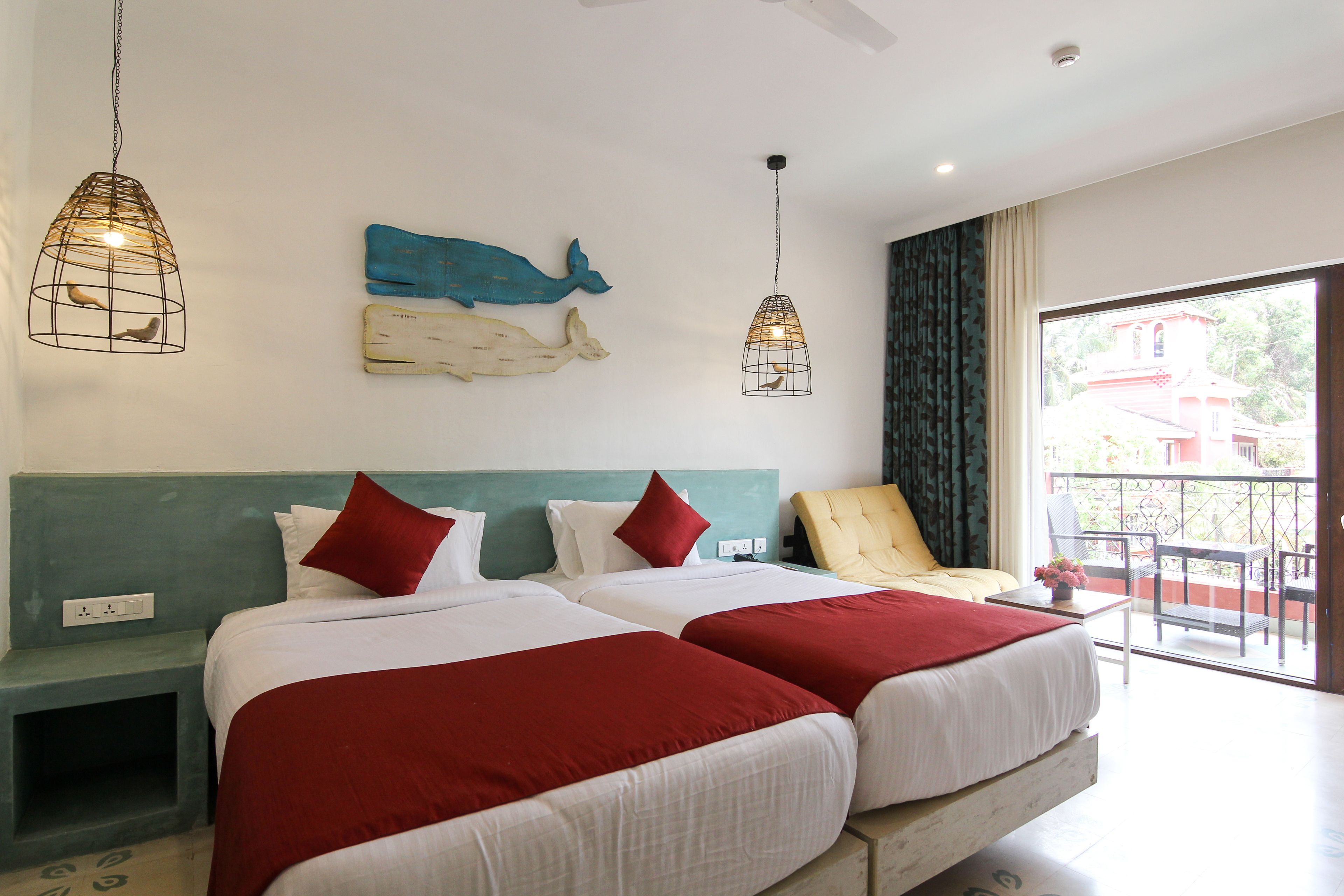 Ein Hotelzimmer mit zwei Betten, einem Balkon mit einem Stuhl sowie Wandbildern von Wal und Robbe.