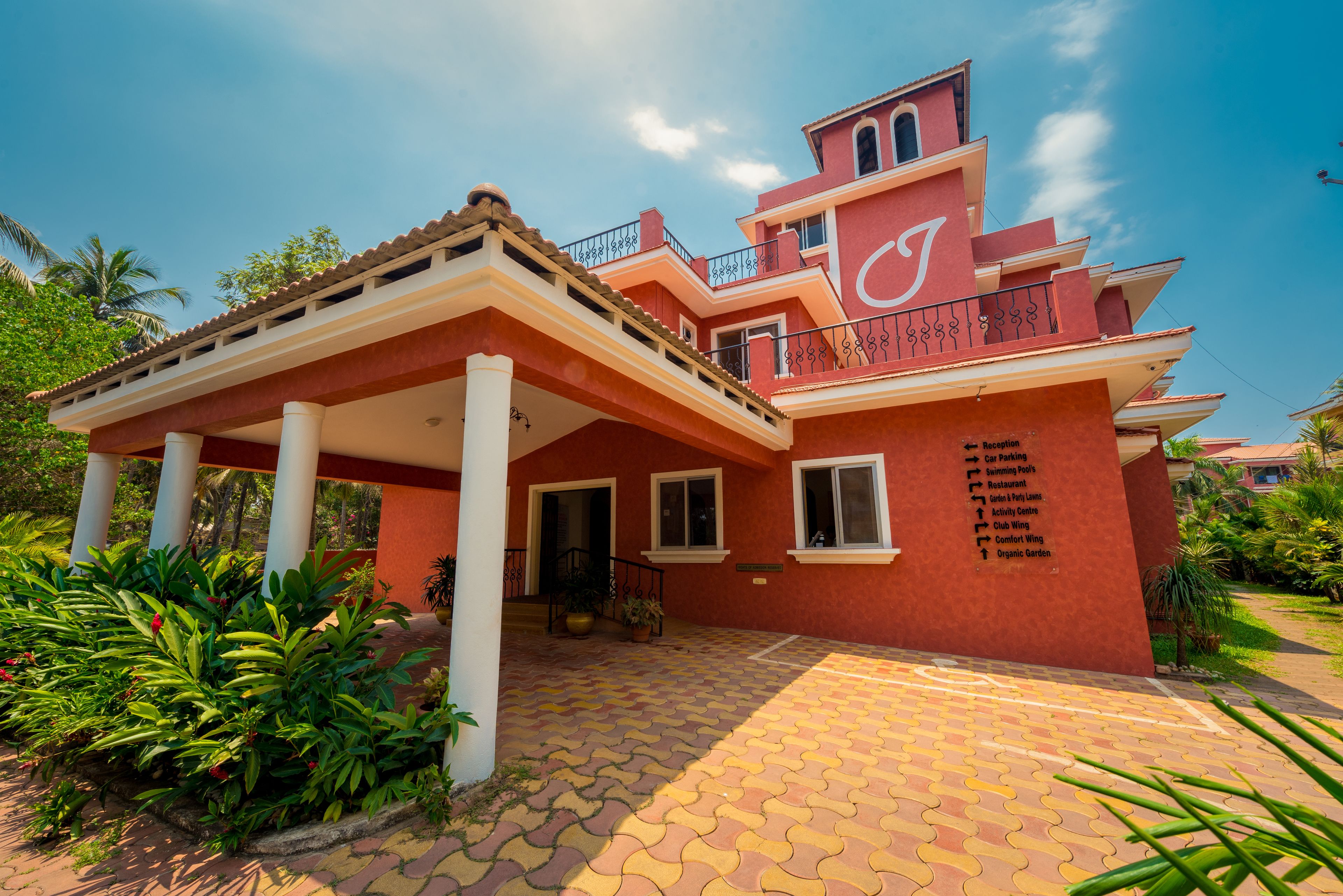 A multi-story building with a red facade, a covered entrance, and a list of amenities including a car park, swimming pool, and restaurant.