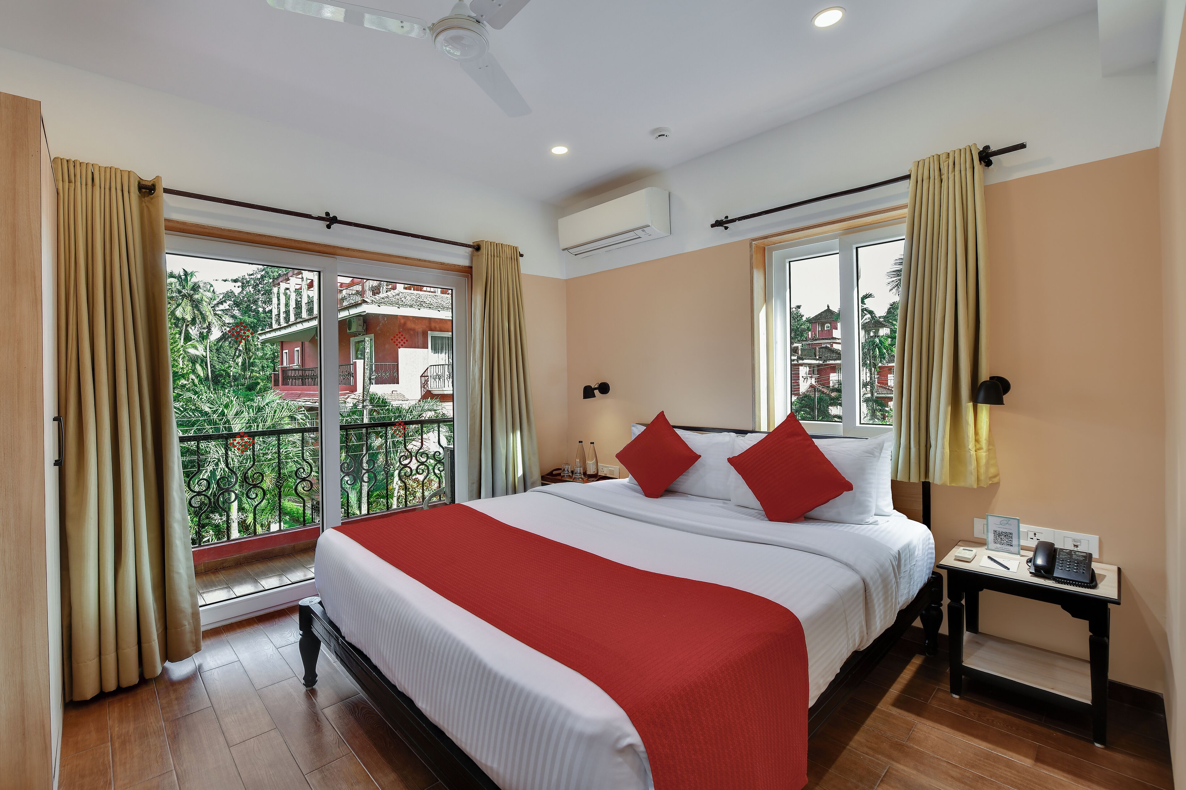 Quarto de hotel com uma cama grande, mesa de cabeceira com telefone e luminária, e vista para uma varanda com cortinas.